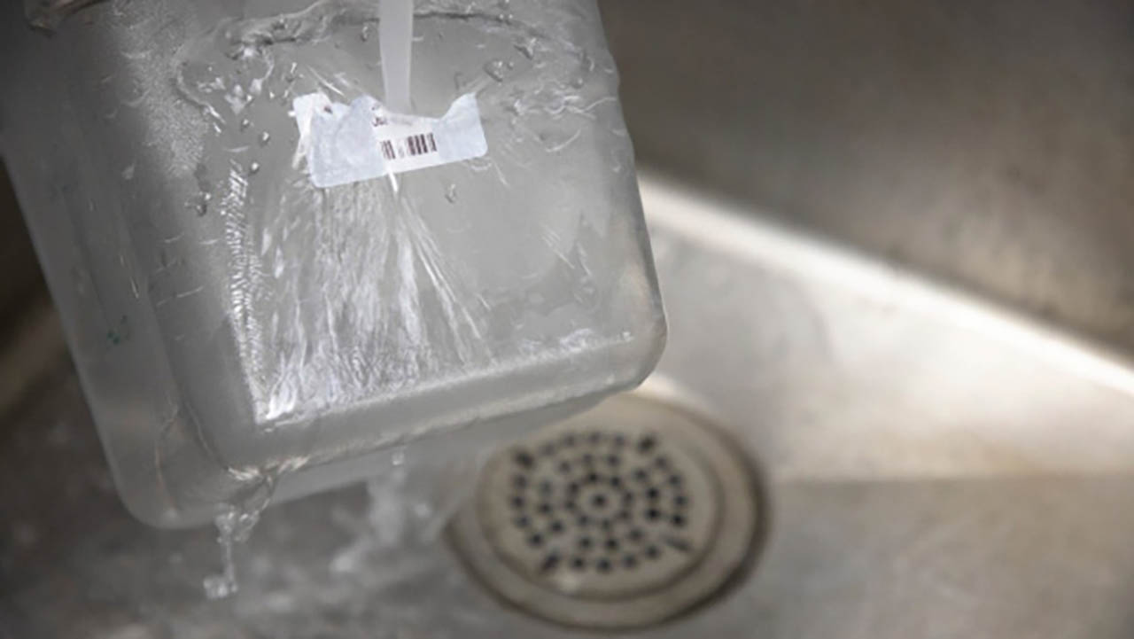 A Zebra 8000D High-Temp Dissolvable Label is washed off a food bin by running water