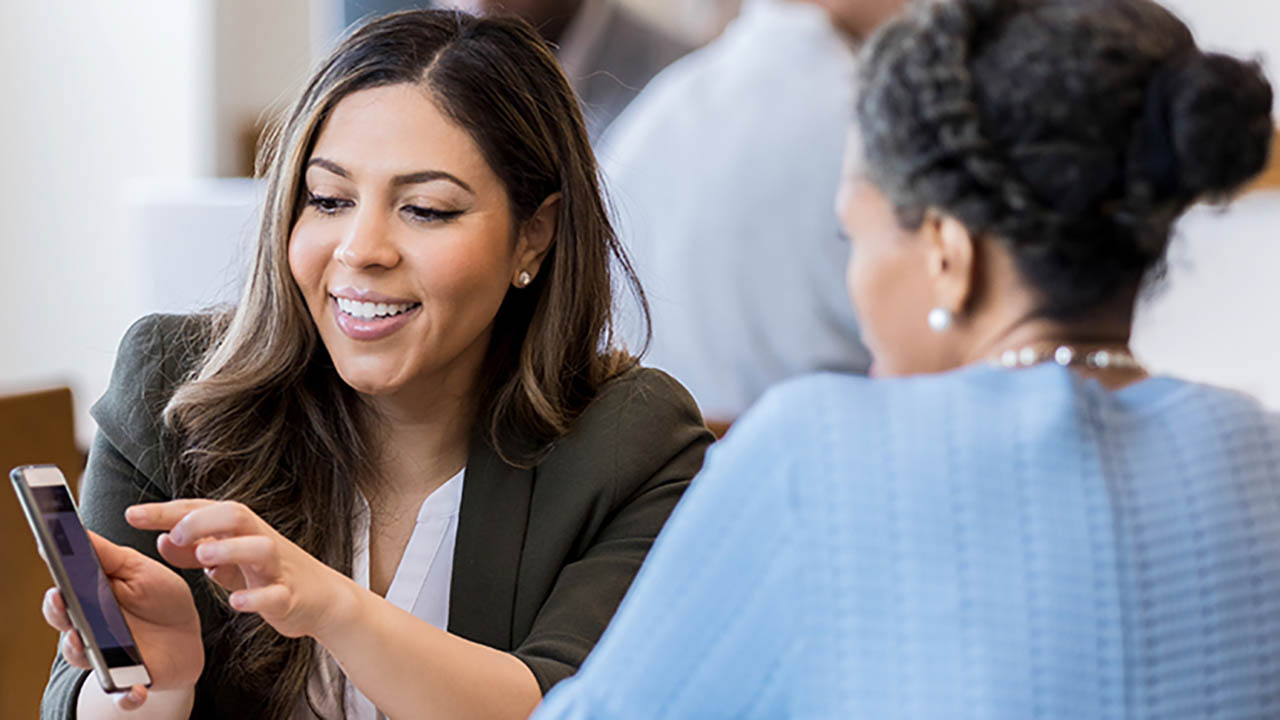 A banking associate shows a customers something on her mobile device