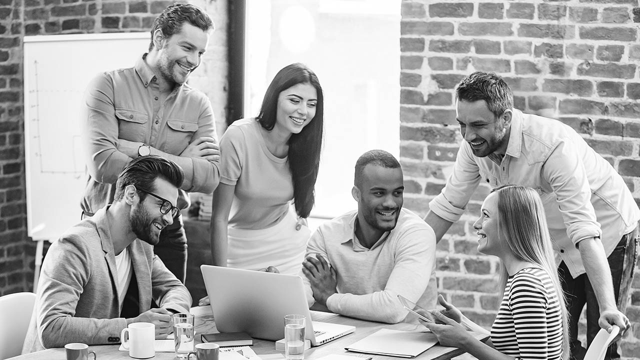 A diverse group of colleagues gather around a computer for a meeting.