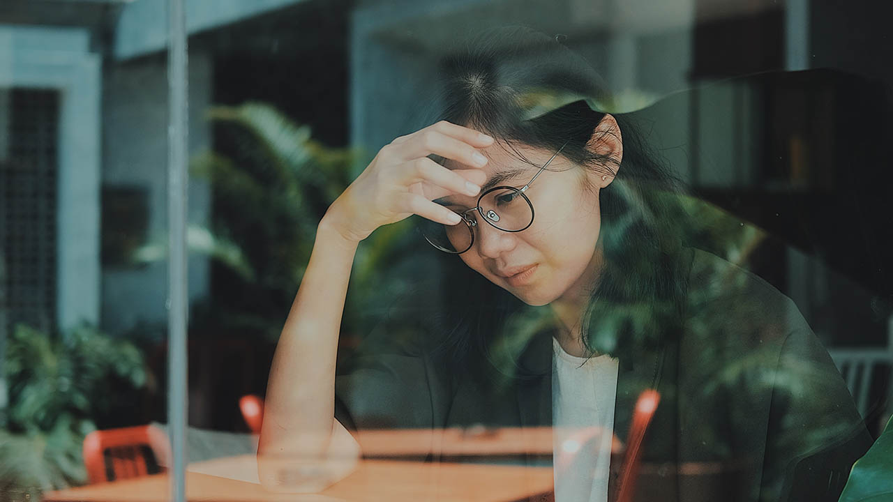 A visibly upset woman sits at a table at a cafe.