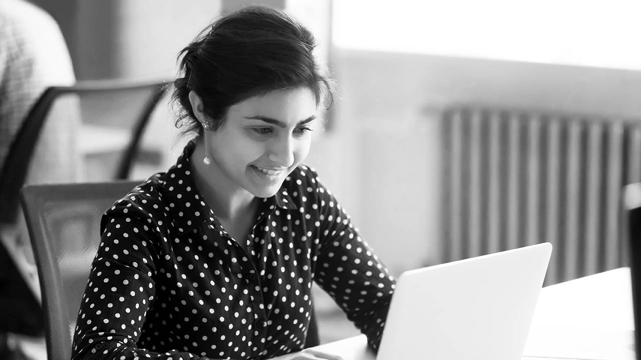 A woman smiles while looking at her laptop