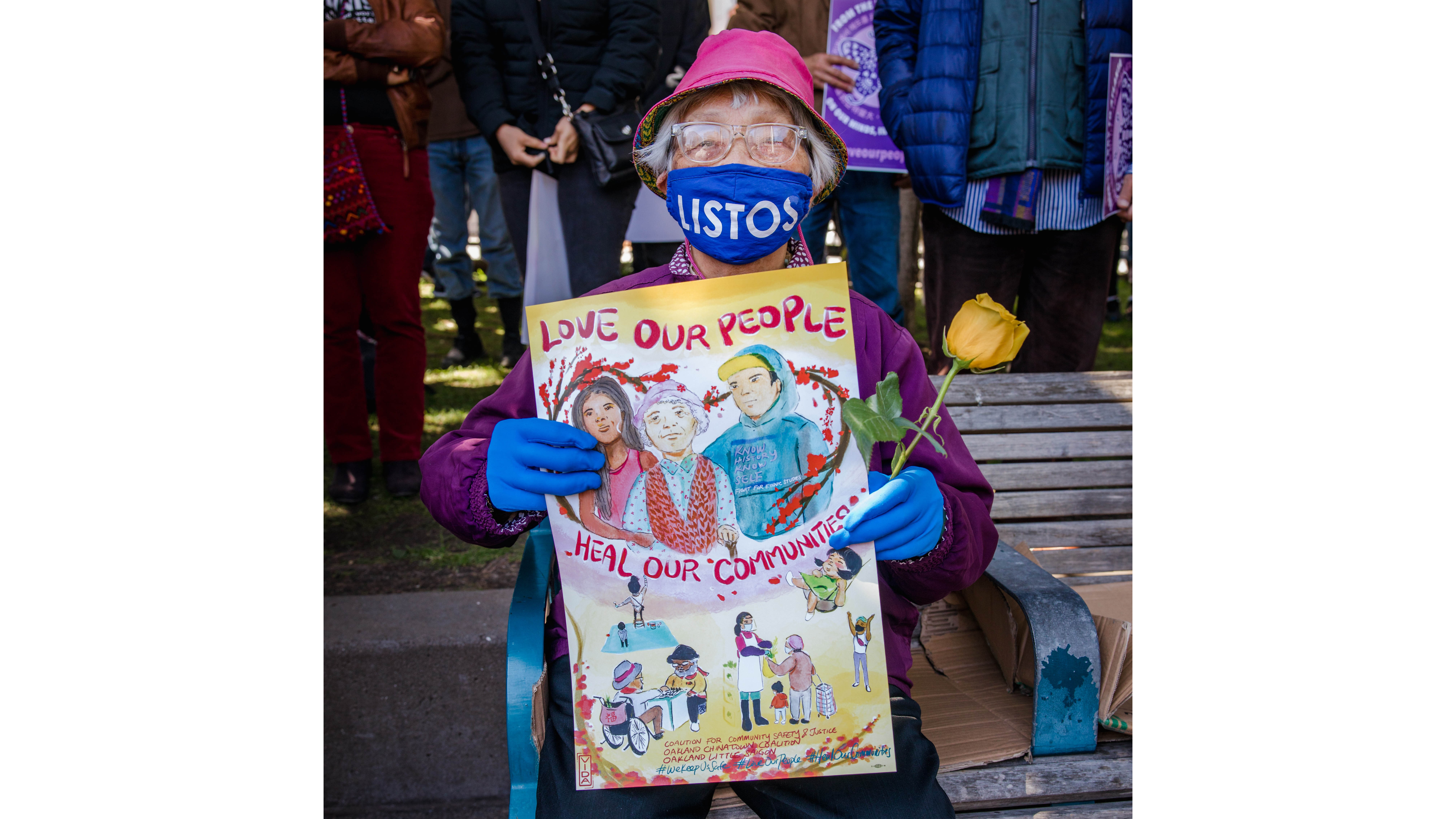 An Asian woman sitting in a wheelchair holds a sign encouraging people to spread love.