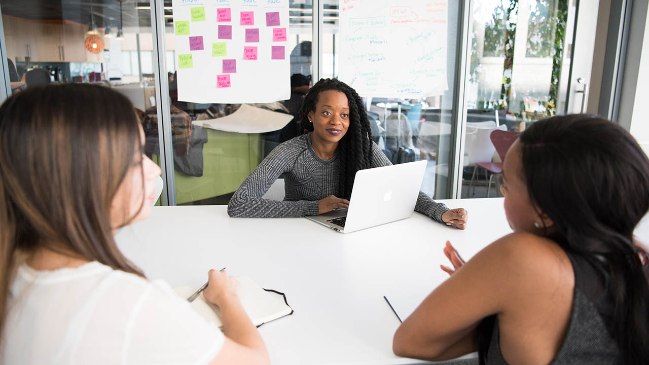 Three women sit at a table reviewing plans