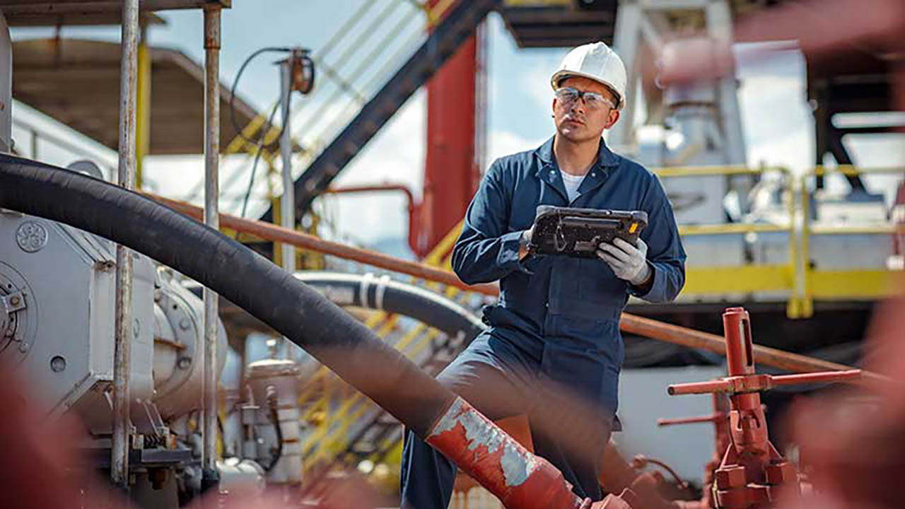 An oil industry worker looks at equipment while holding a Zebra rugged tablet