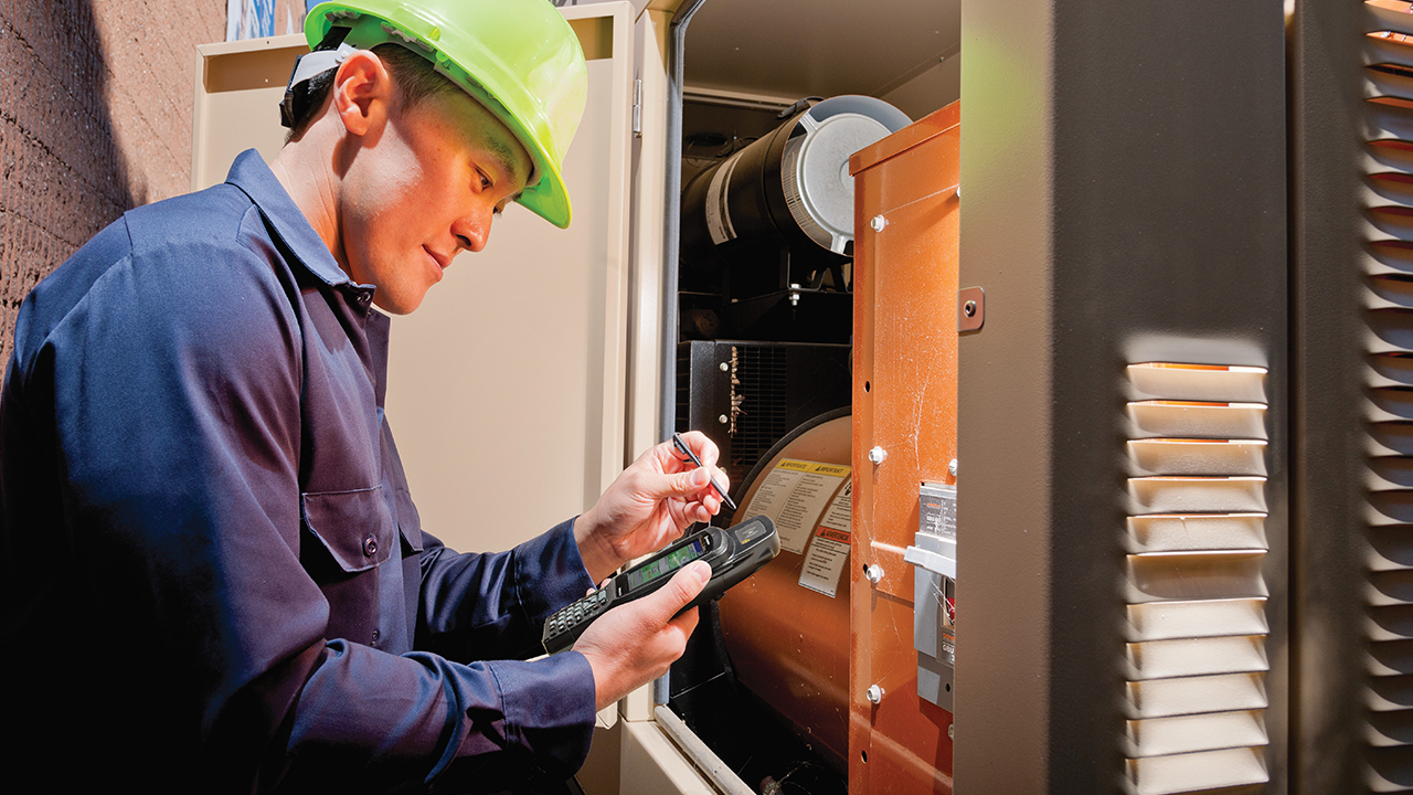 A field technician looks at his mobile computer for guidance while inspecting a piece of electrical equipment.