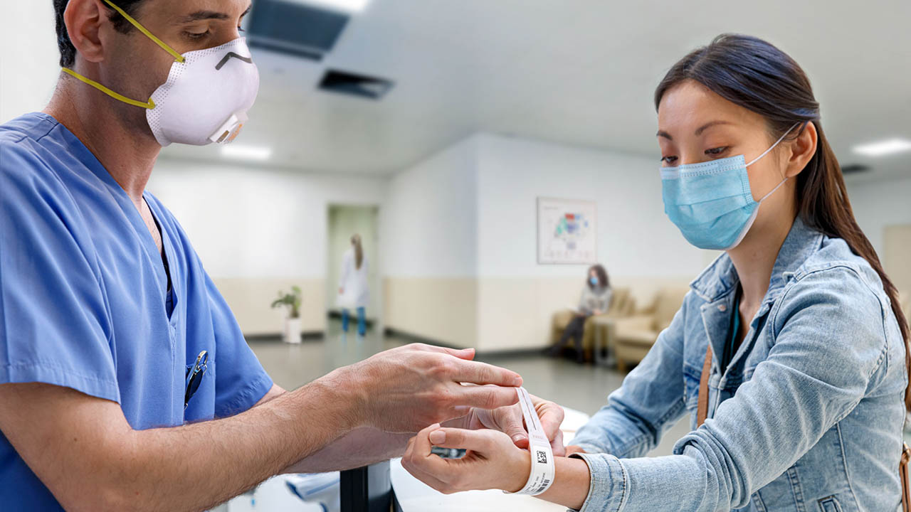 A nurse puts a wristband ona patient during the admissions process