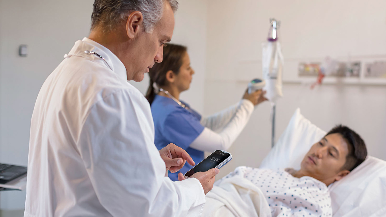 A doctor uses a clinical smartphone to pull up a patient's records bedside.