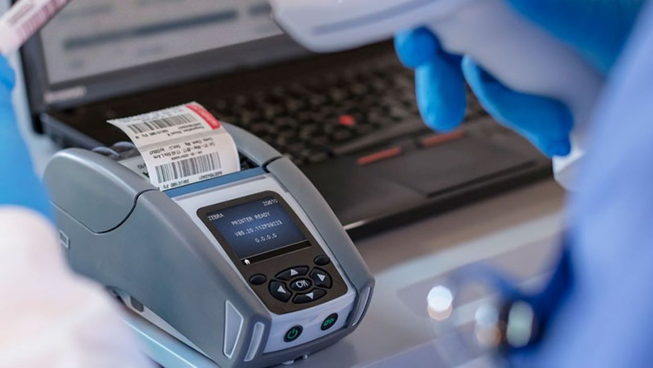 A Zebra mobile printer generates a label for a specimen collection container at the patient's bedside