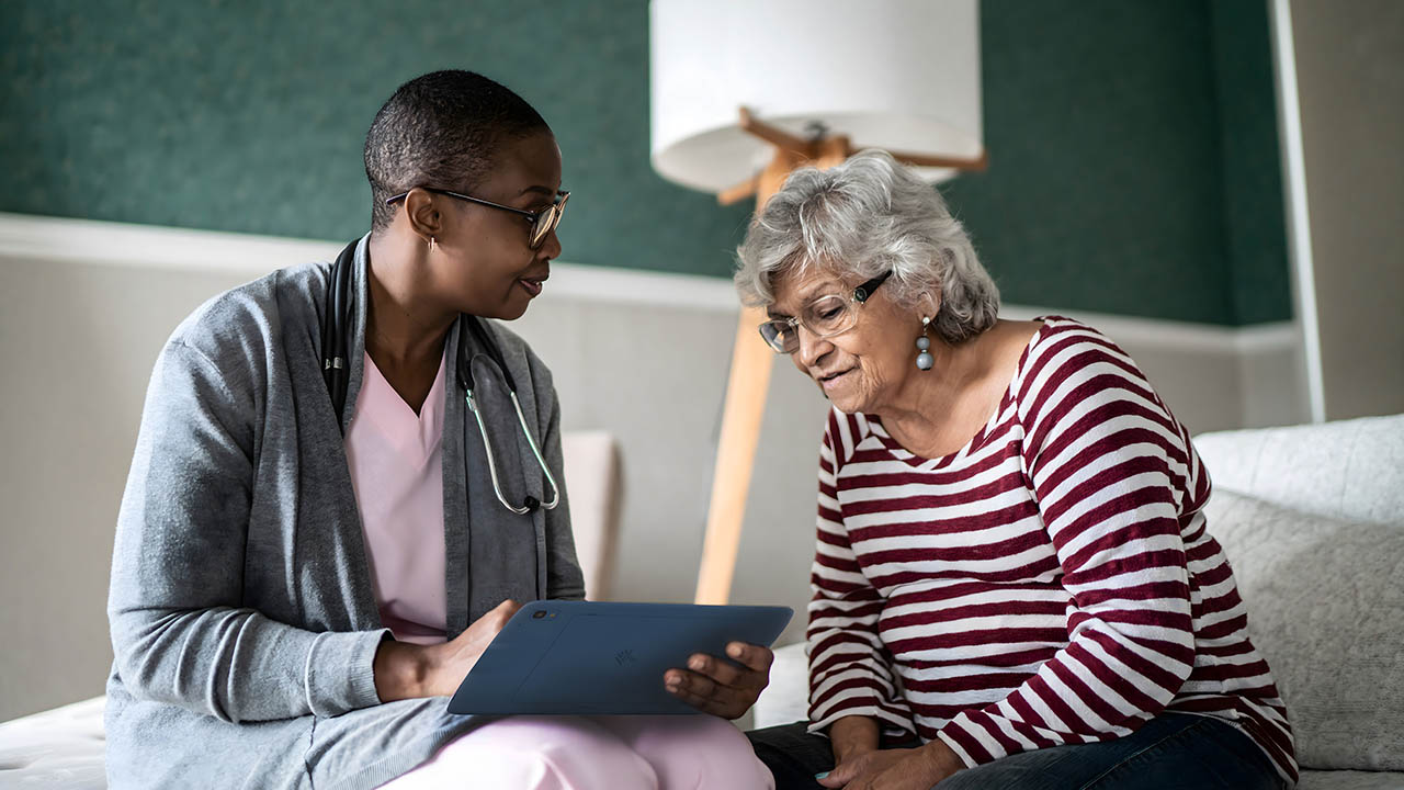 A home health nurse consults with a patient while lookning at a Zebra healthcare tablet in the patient's living room