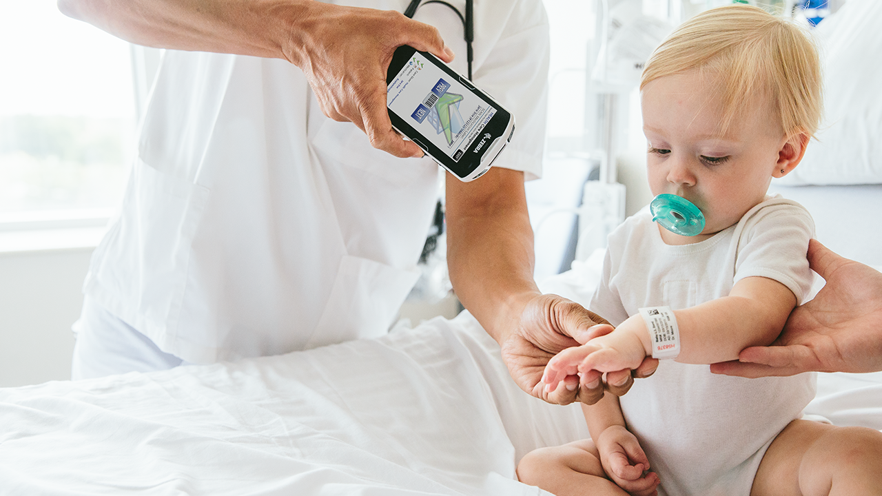 A clinician uses a handheld mobile computer to scan the barcode on a young child's wristband