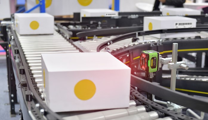 Boxes on a conveyor belt being scanned by a fixed scanner using machine vision.