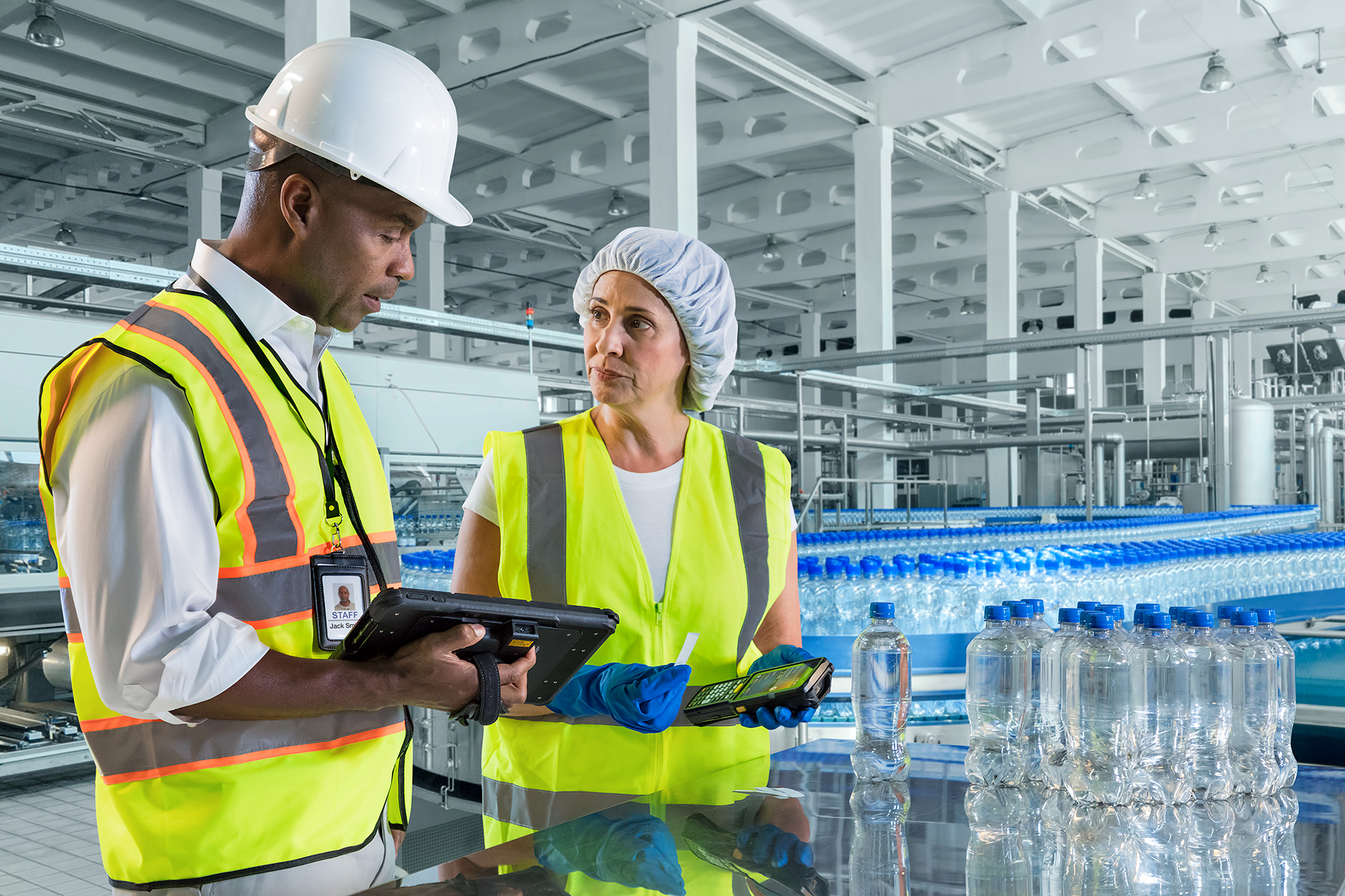 Two workers reviewing notes on their rugged mobile computers on the manufacturing factory floor