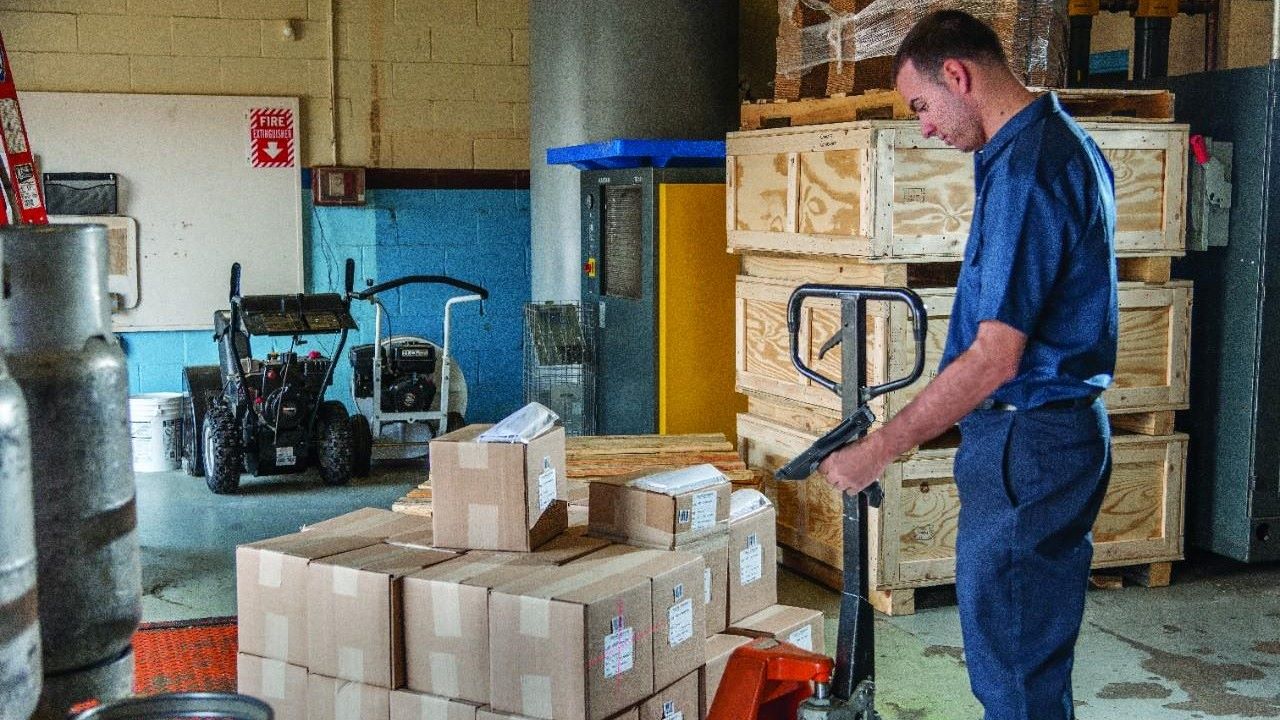 A man uses a mobile computer to scan boxes on a pallet in a warehouse.