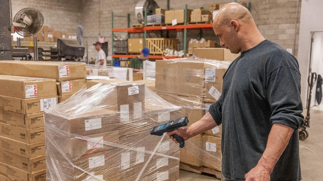 A warehouse worker scans the barcode on a pallet of boxes wrapped in plastic