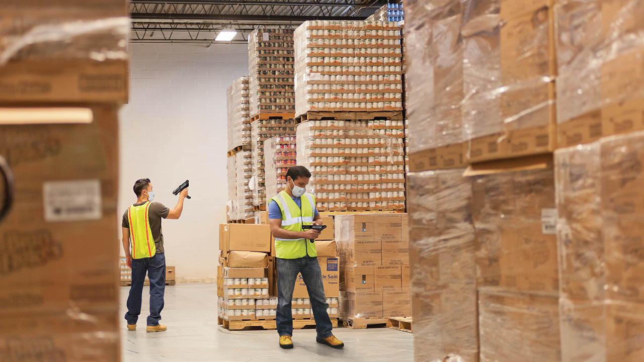 Two warehouse workers scan inventory while maintaining social distance