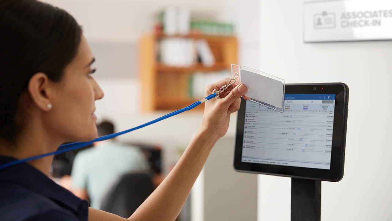 A retail store associate clocking in using their badge on a Zebra tablet running Reflexis software