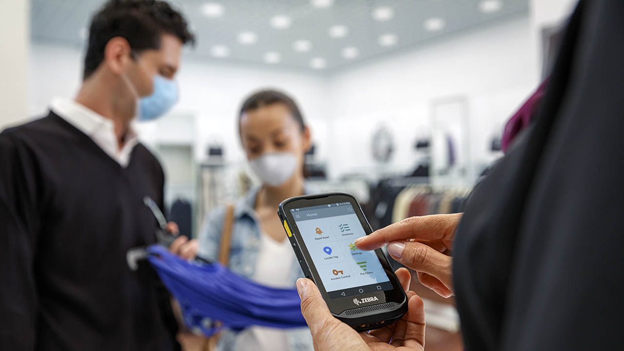 A retail store associate looks at her handheld mobile computer screen to pull up item info for two customers