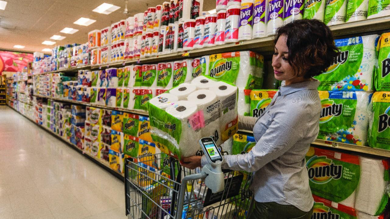 A woman uses a smartphone-like device to scan paper towels and add them to her mobile (self-checkout) cart
