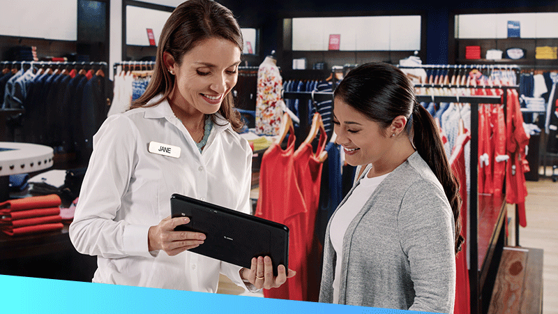Female retail associate using rugged tablet to assist customer in apparel store