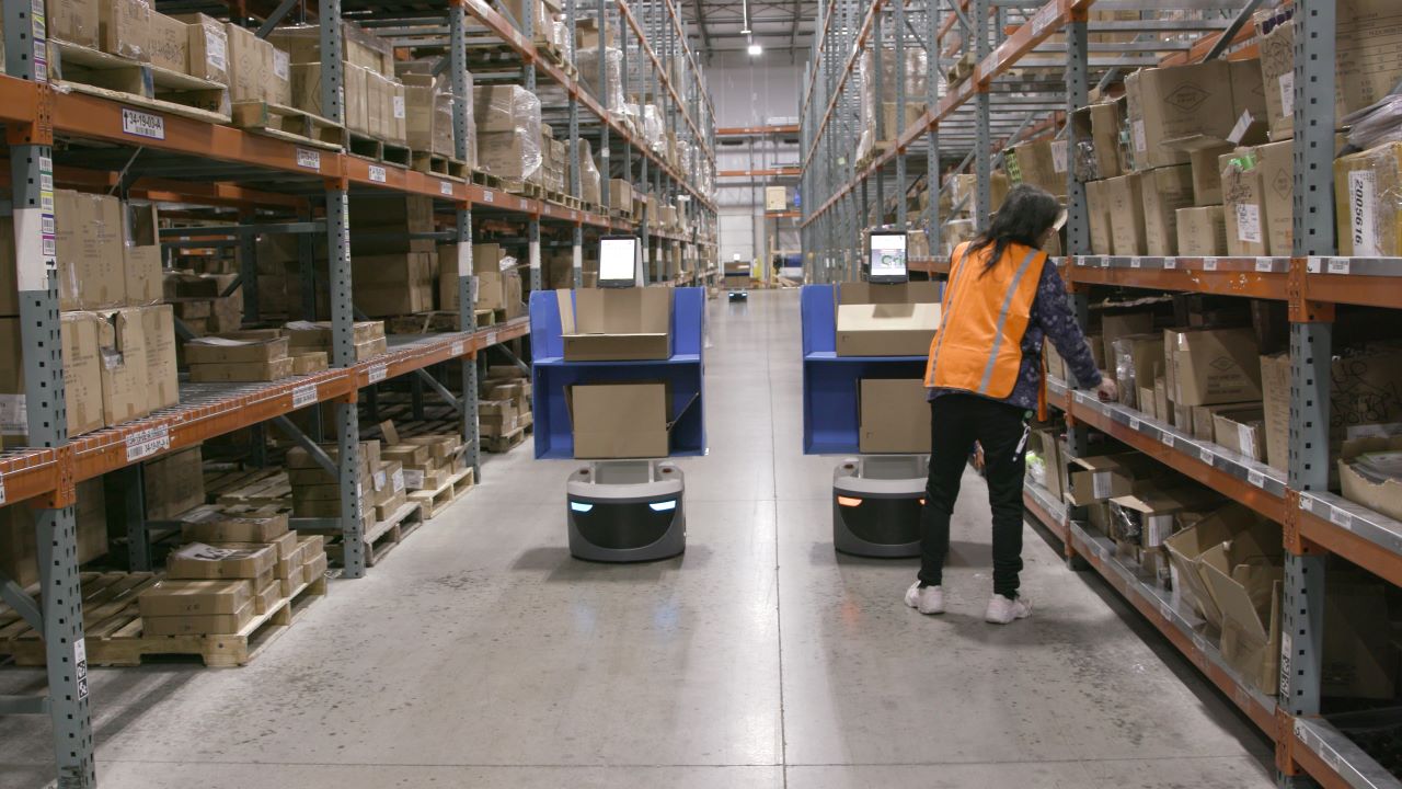 A worker collaborates with a Locus Robotics co-bot to pick inventory in a warehouse