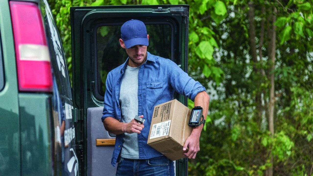 A delivery driver scans a package using a ring scanner connected to a Zebra TC52 Android touch computer that he's wearing on his arm.