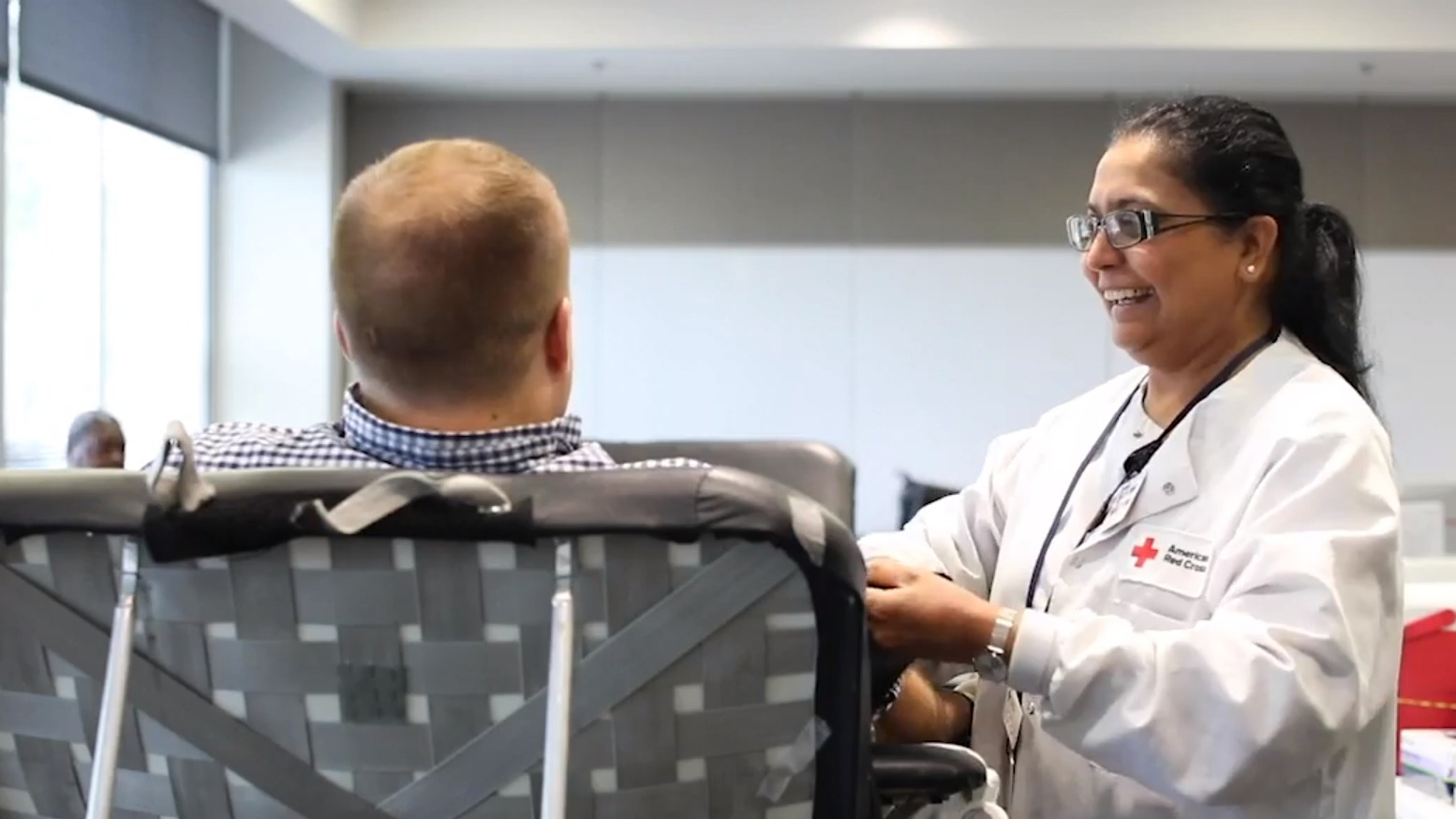 A man sits in a chair while a Red Cross volunteer draws blood