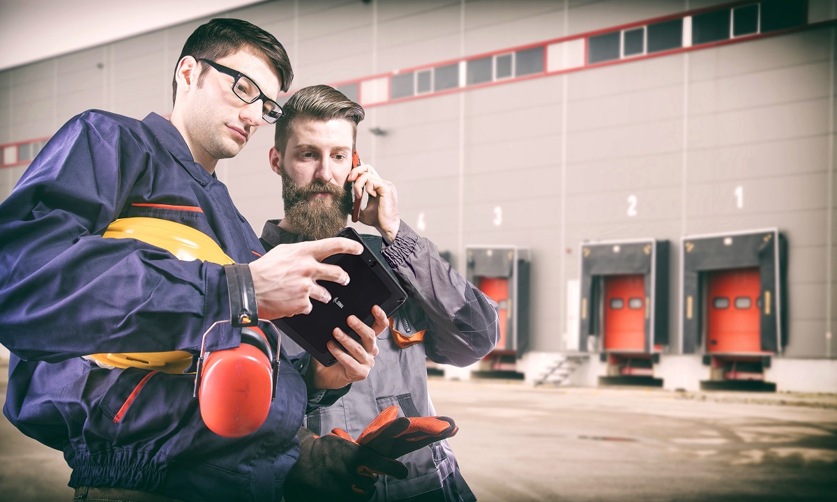 Two male workers using mobile technology on the loading dock to coordinate transportation and logistics activities.