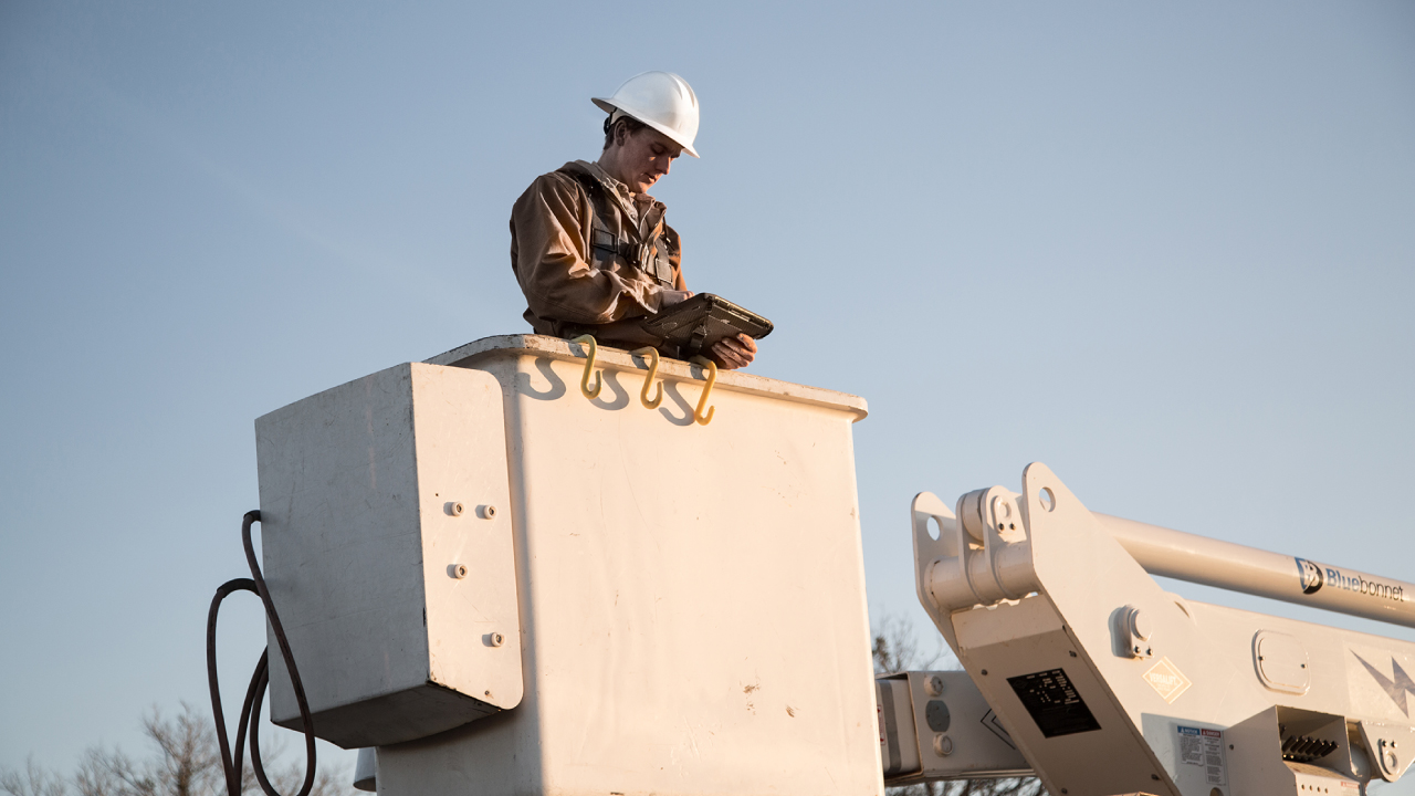 A field technician for a utility company looks at his rugged tablet while in a lift truck bucket.