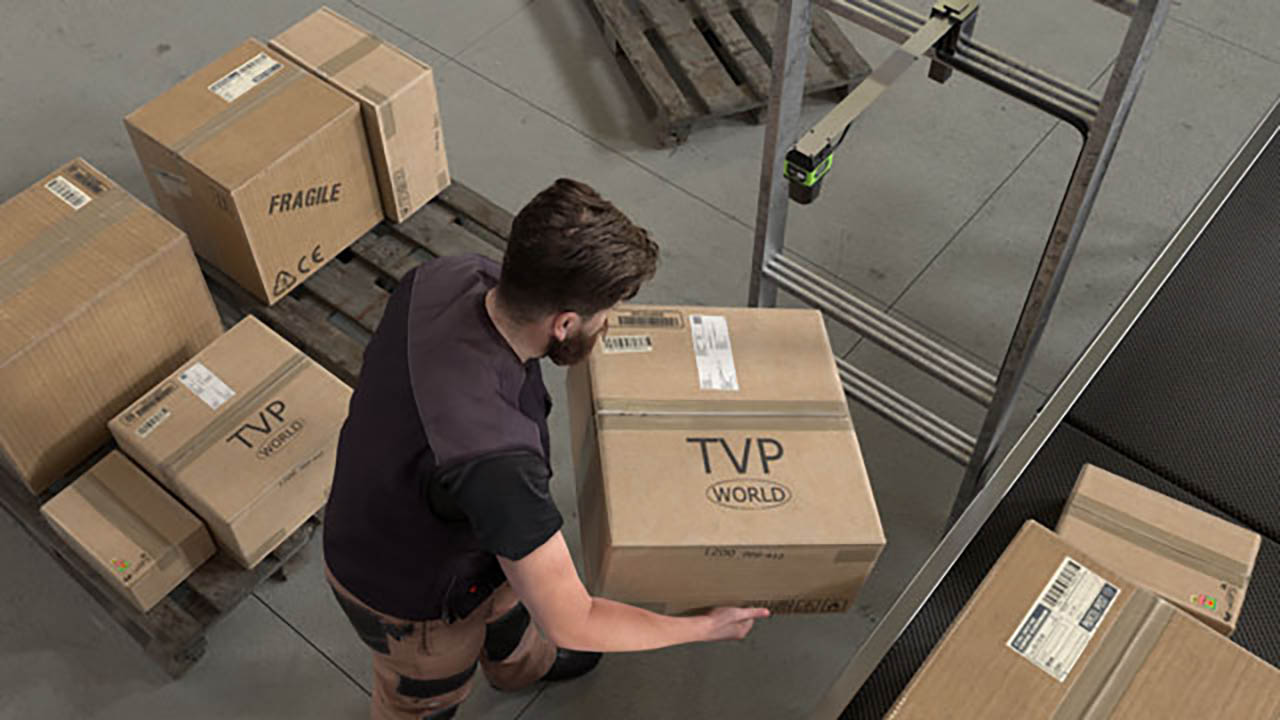 A warehouse worker uses a fixed industrial scanner to scan a label on a box.