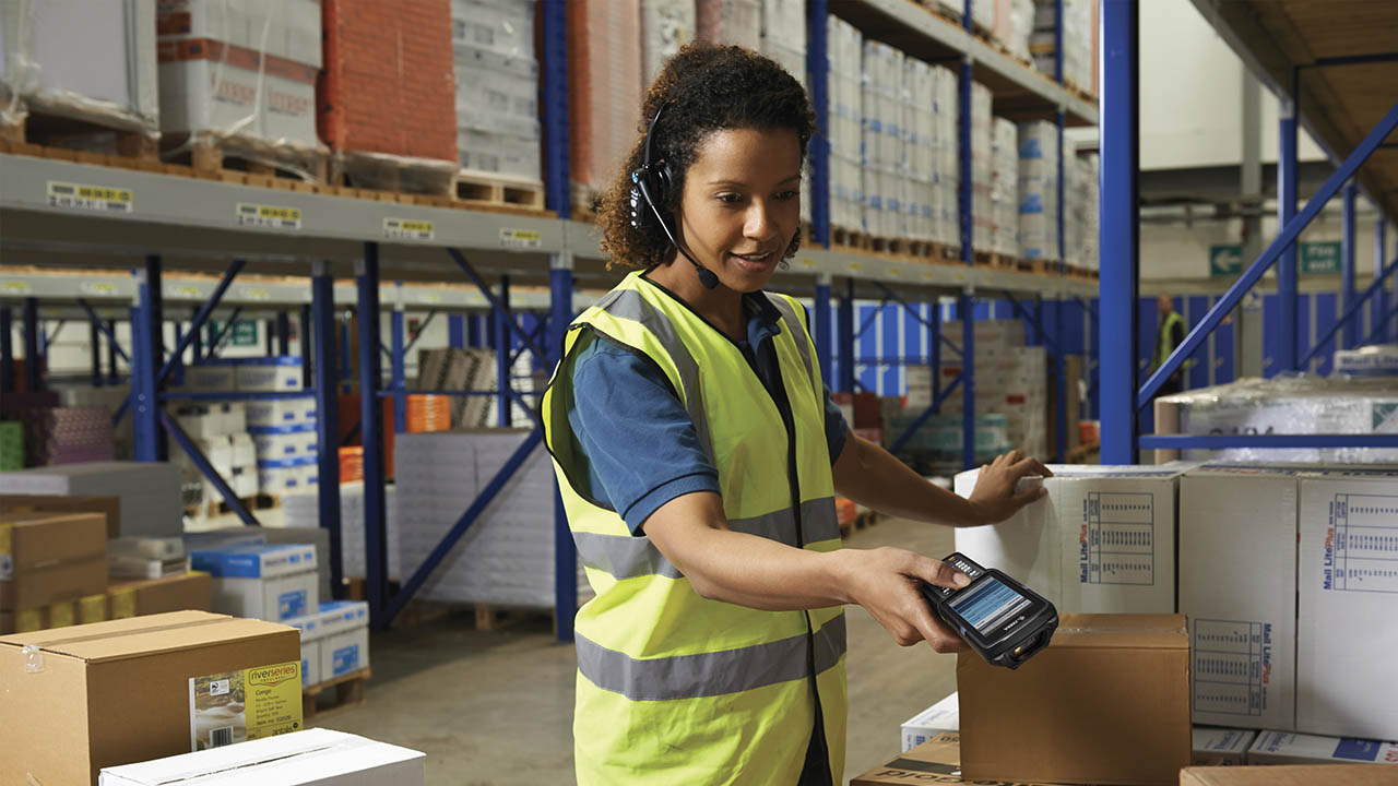 A warehouse associate uses a Zebra handheld mobile computer and voice technology to pick an order