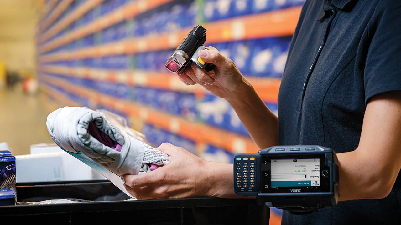 A warehouse worker scans the barcode on an item using a ring scanner connected to a wrist-worn mobile computer terminal