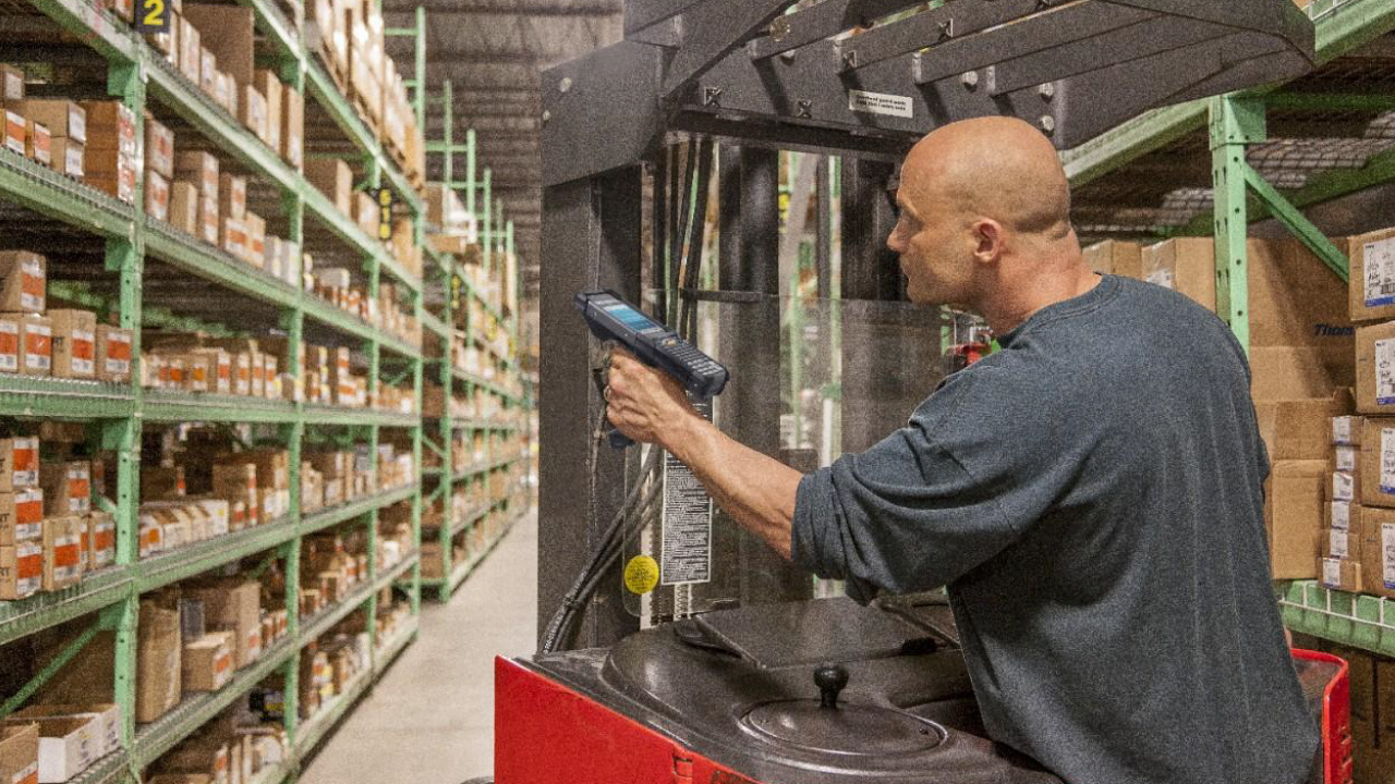 A male warehouse worker uses a handheld mobile computer to scan an item on a shelf