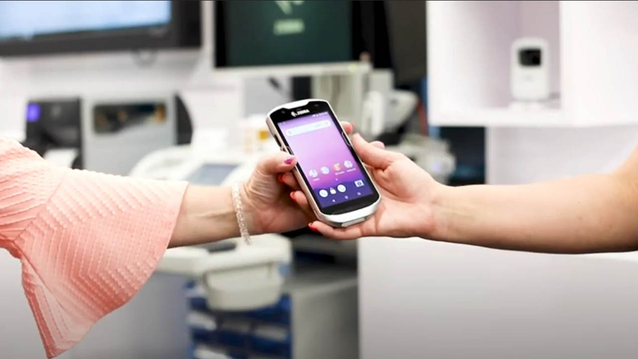 A healthcare provider hands a clinical smartphone off to another worker