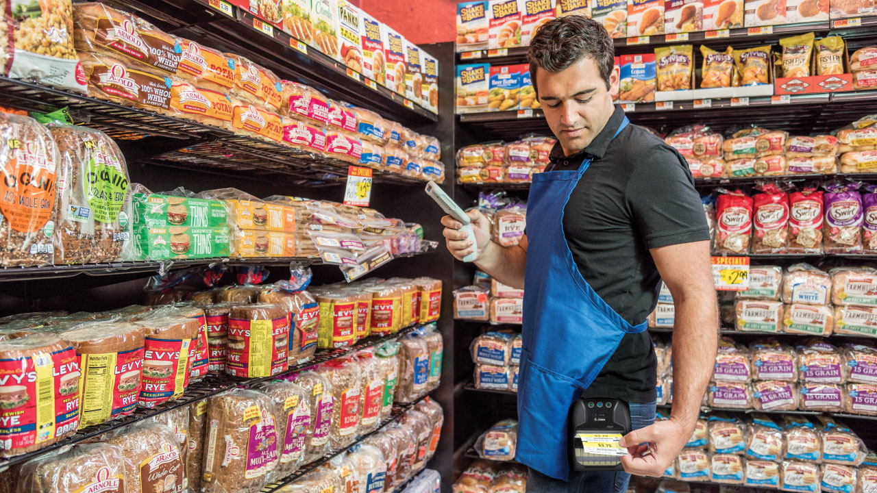 A grocery store worker prints up a price tag for a loaf of bread using a mobile printer