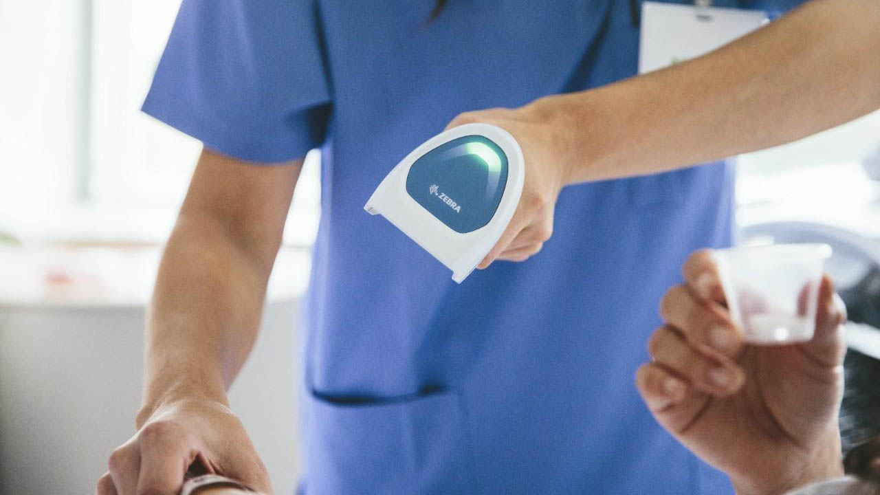 A Zebra DS8100HC scanner is used by a nurse to scan a patient's wristband