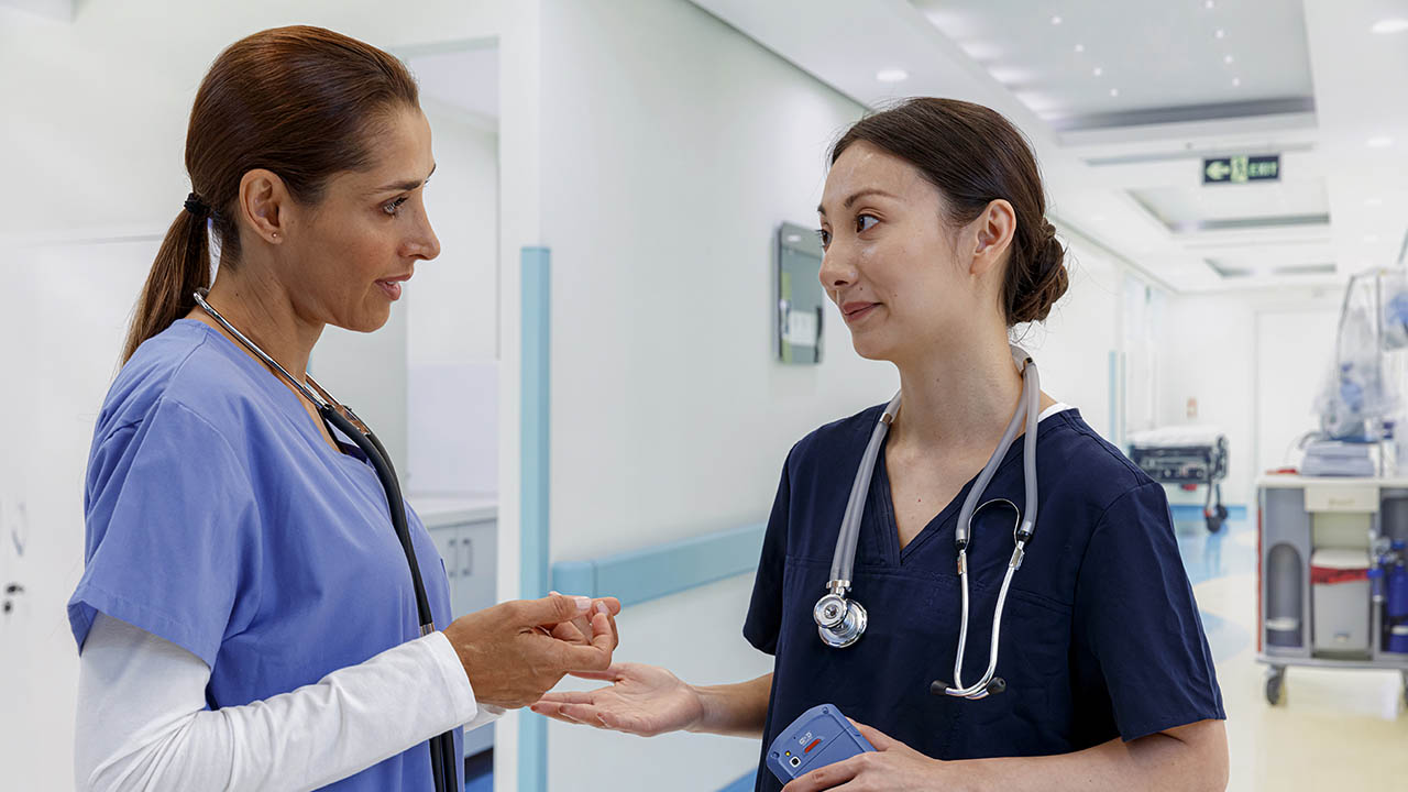 Two nurses talk in a hospital hallway