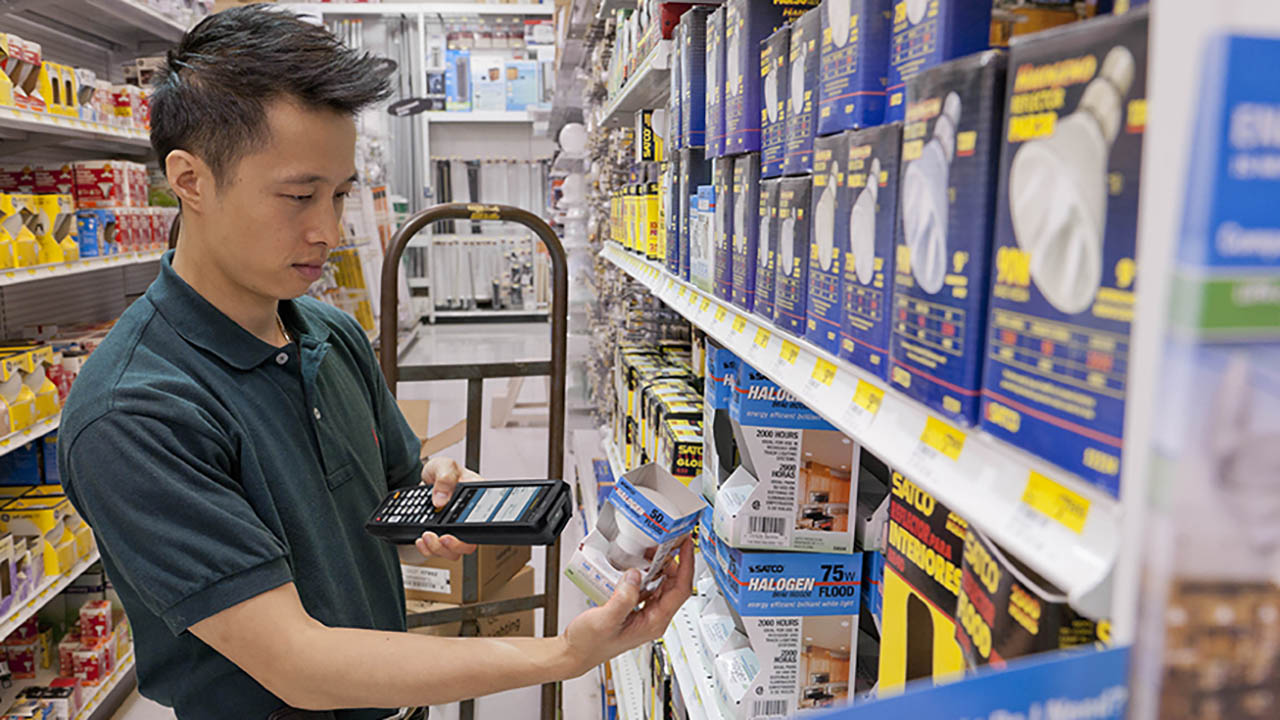 A hardware store associate scans a light bulb before putting it on the shelf