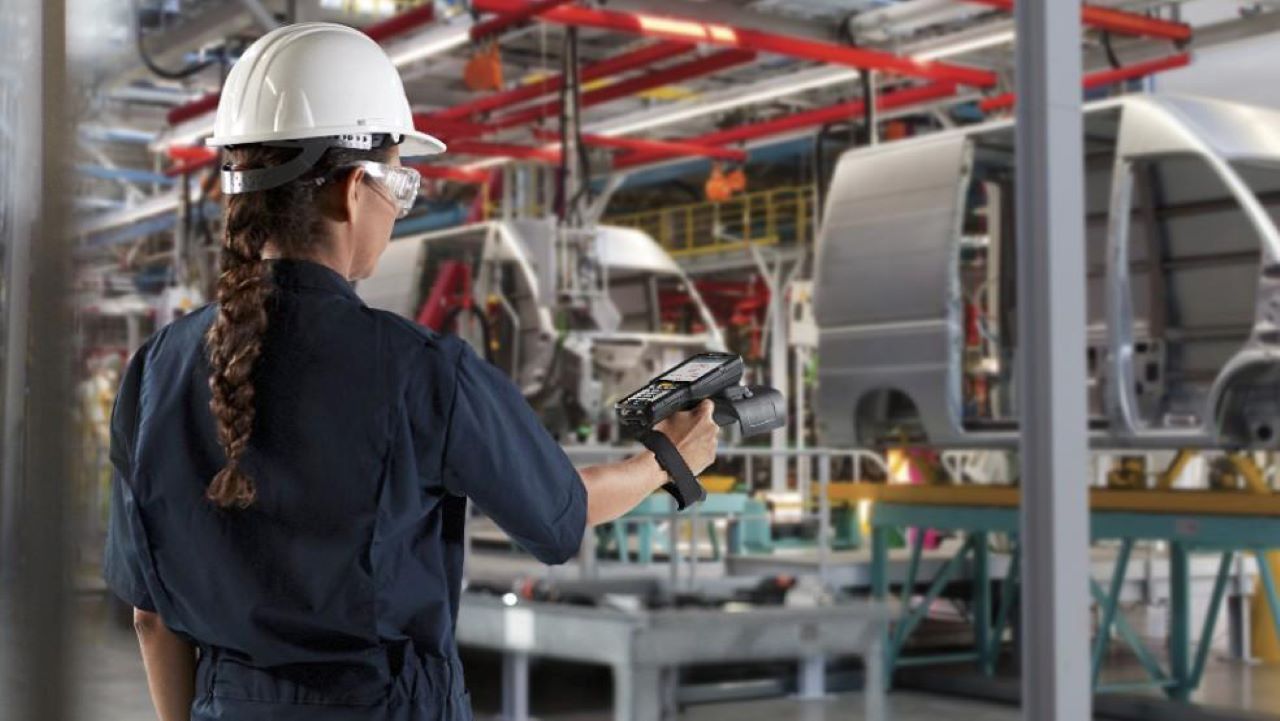 A manufacturing worker uses a Zebra handheld RFID mobile computer to read tags on vehicles moving down the line. 