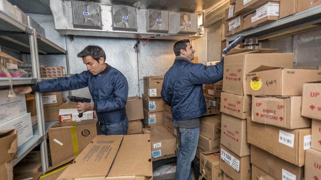Two warehouse workers scan inventory while maintaining social distance