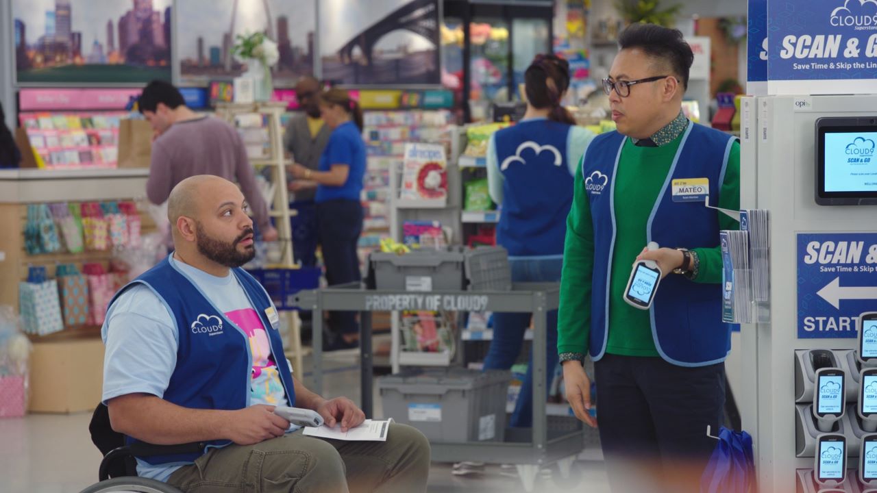 Two members of the cast of the American TV show Superstore stand next to personal shopping solution display with Zebra mobile computers in hand