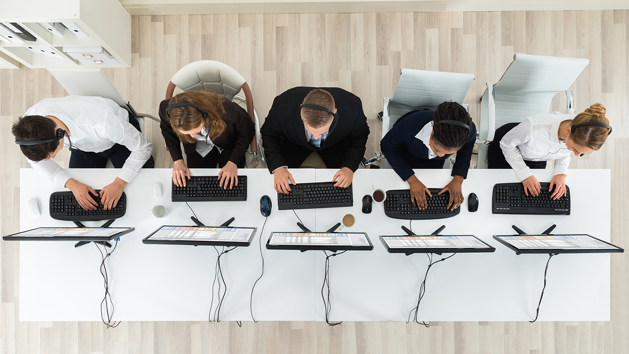 Five IT team members sit in a row at computer stations