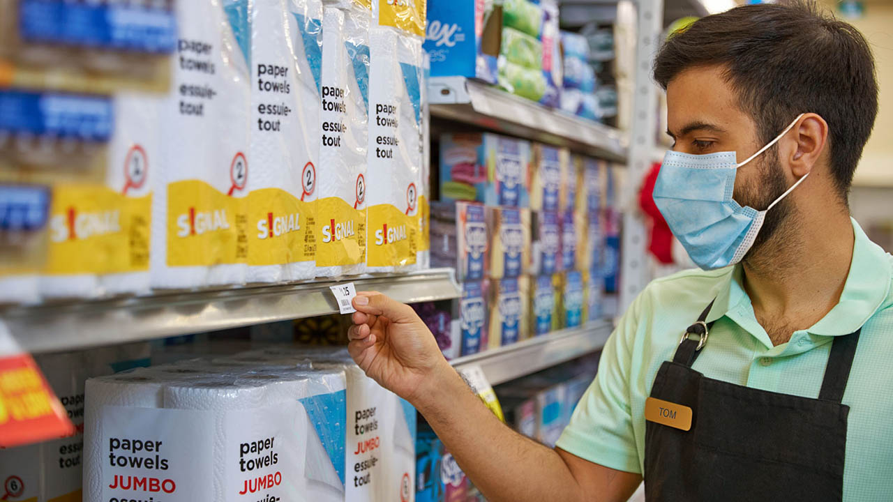 A grocery store associate looks at a shelf price tag.