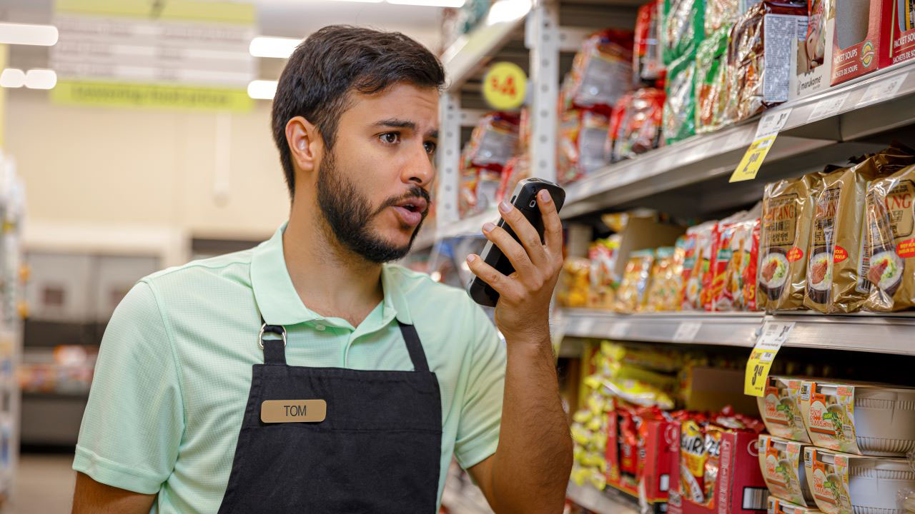 A grocery store associate uses a Zebra TC52 with push-to-talk to communicate with a colleague while looking for an item