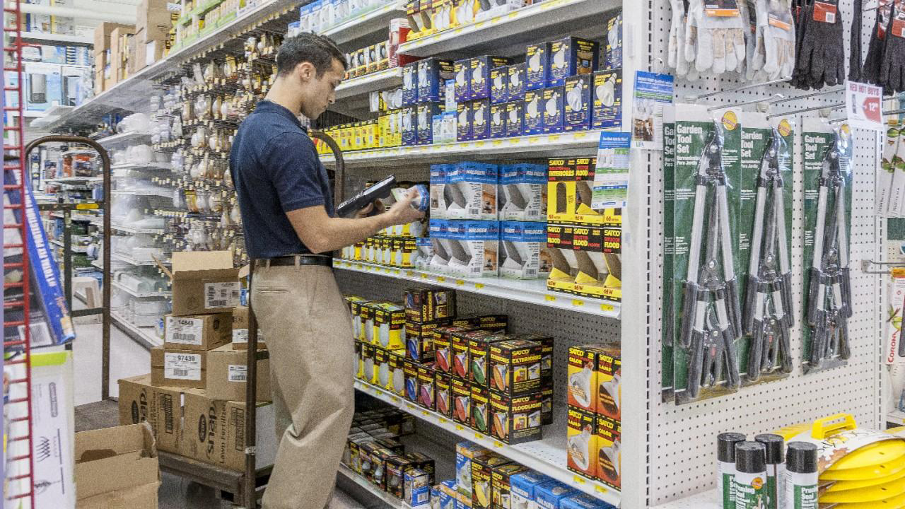 A male stores associate scans cans off vegetables while managing inventory