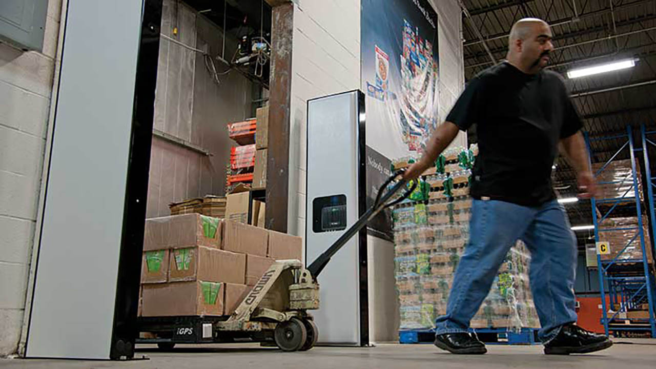 A warehouse worker pulls a cart loaded with boxes past a Zebra FX9600 fixed RFID reader in a warehouse