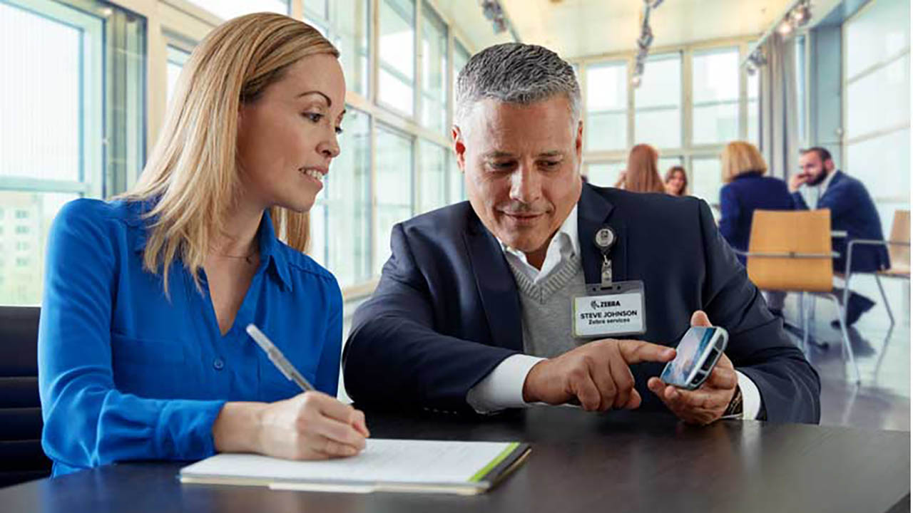 A professional services consultant shows a woman a custom software application on a handheld mobile computer