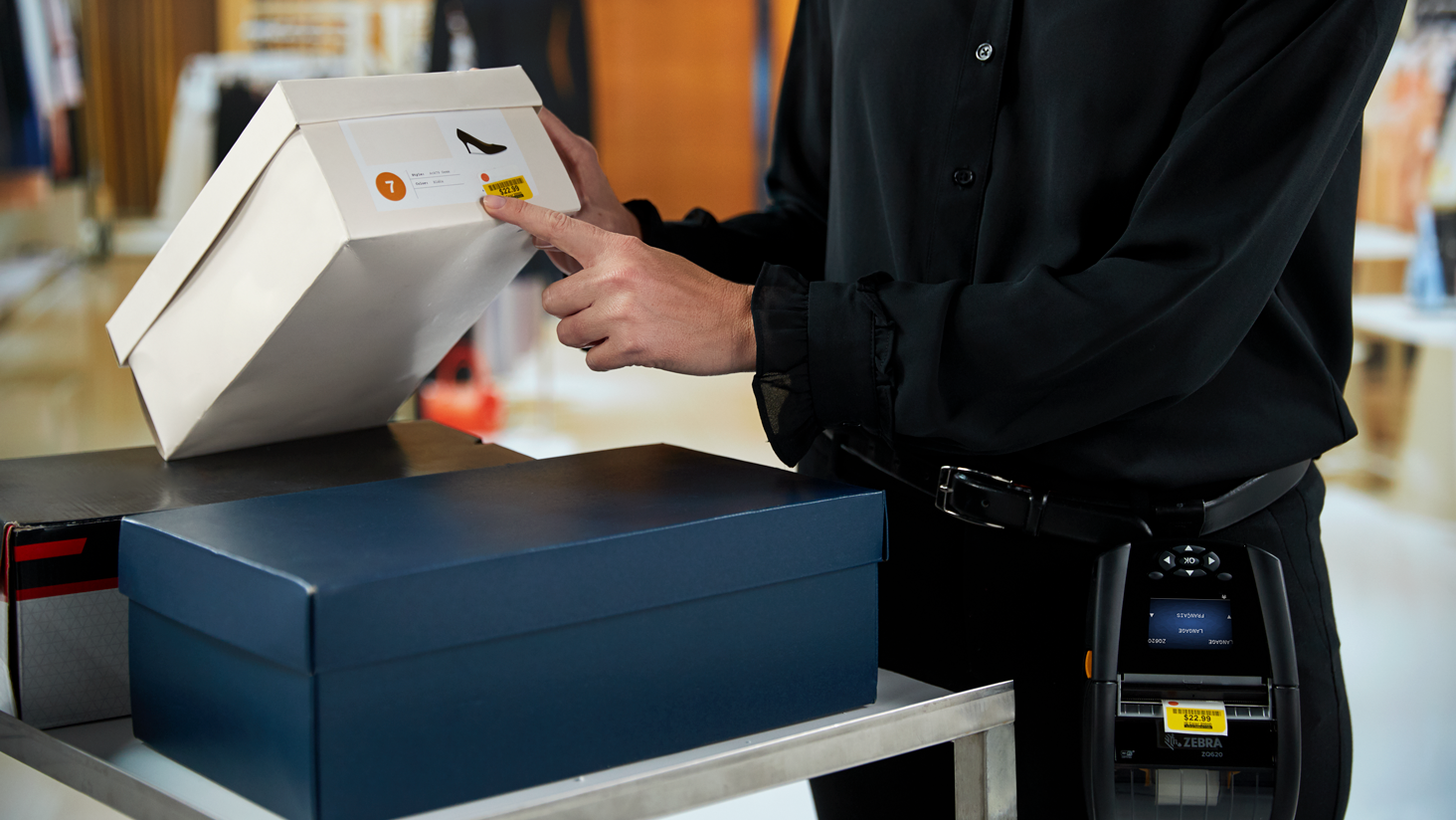 A female retail associate prints a new price tag for a shoe box using a mobile printer