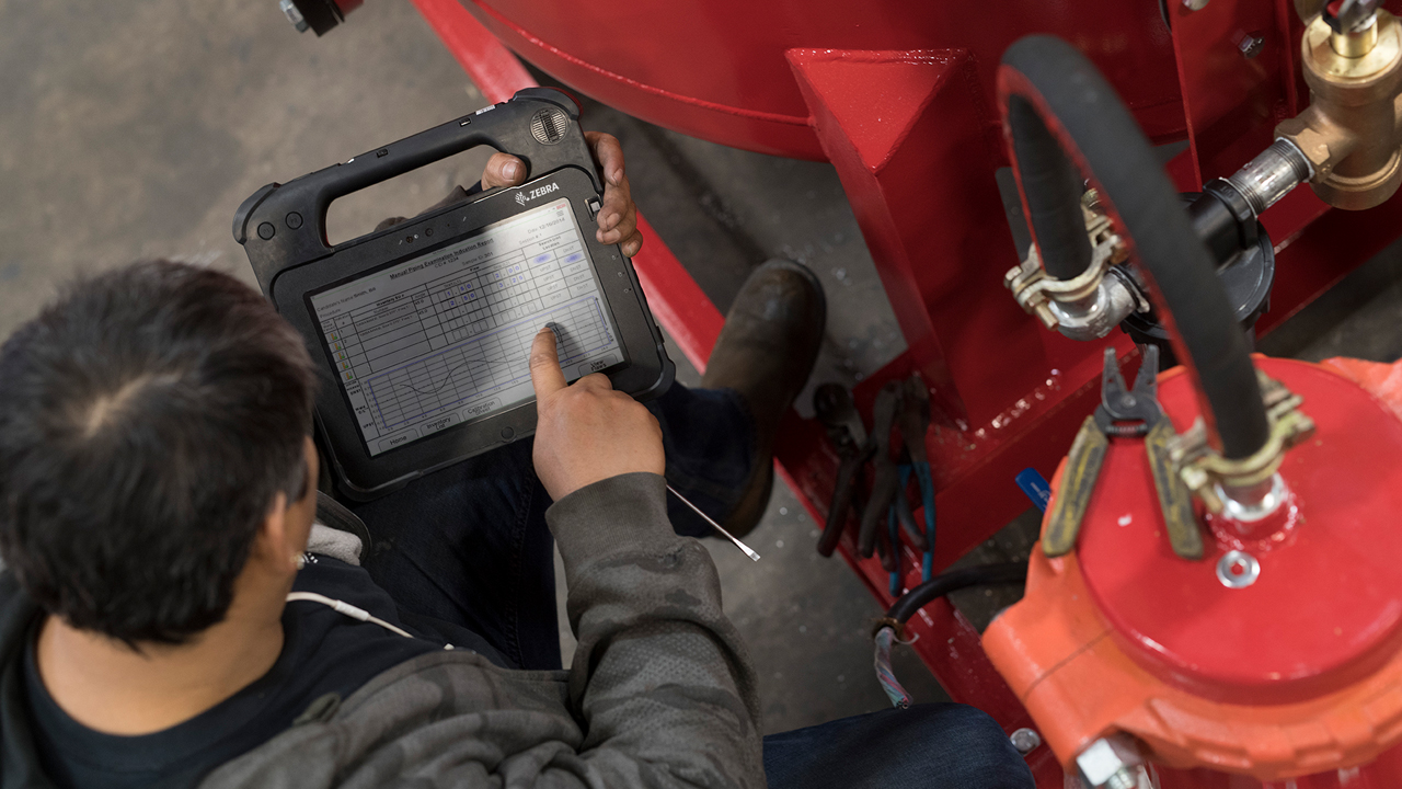 A field technician looks at his rugged tablet screen for instructions on how to service a piece of equipment