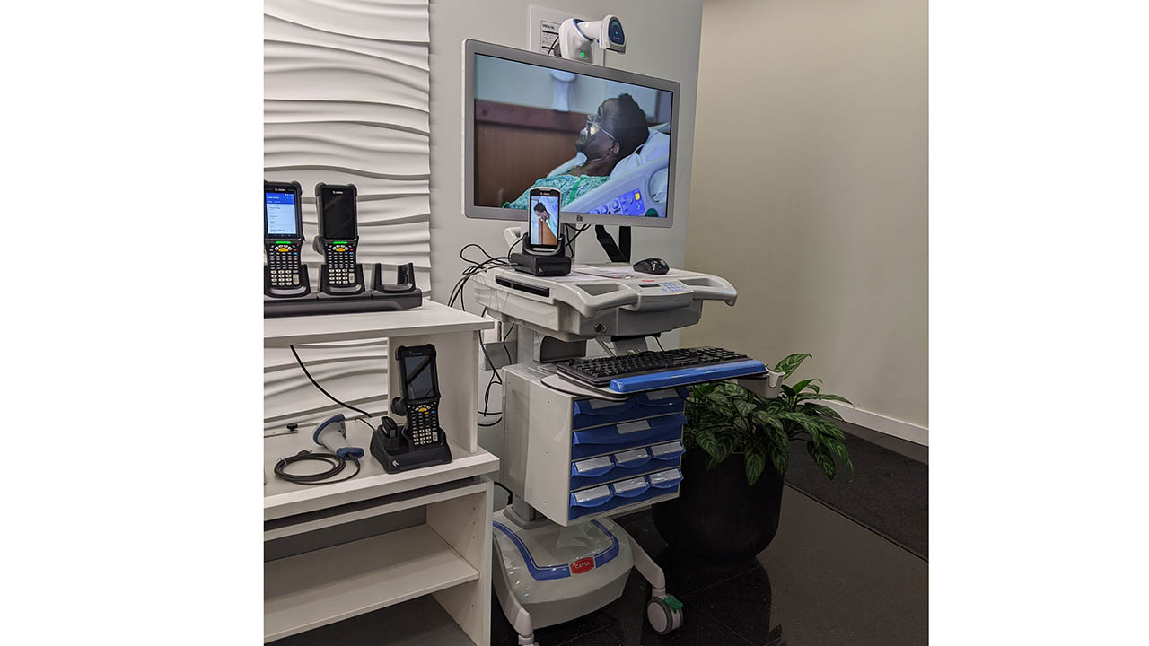 A patient is remotely monitored via mobile computers and screens on a nurse's cart.