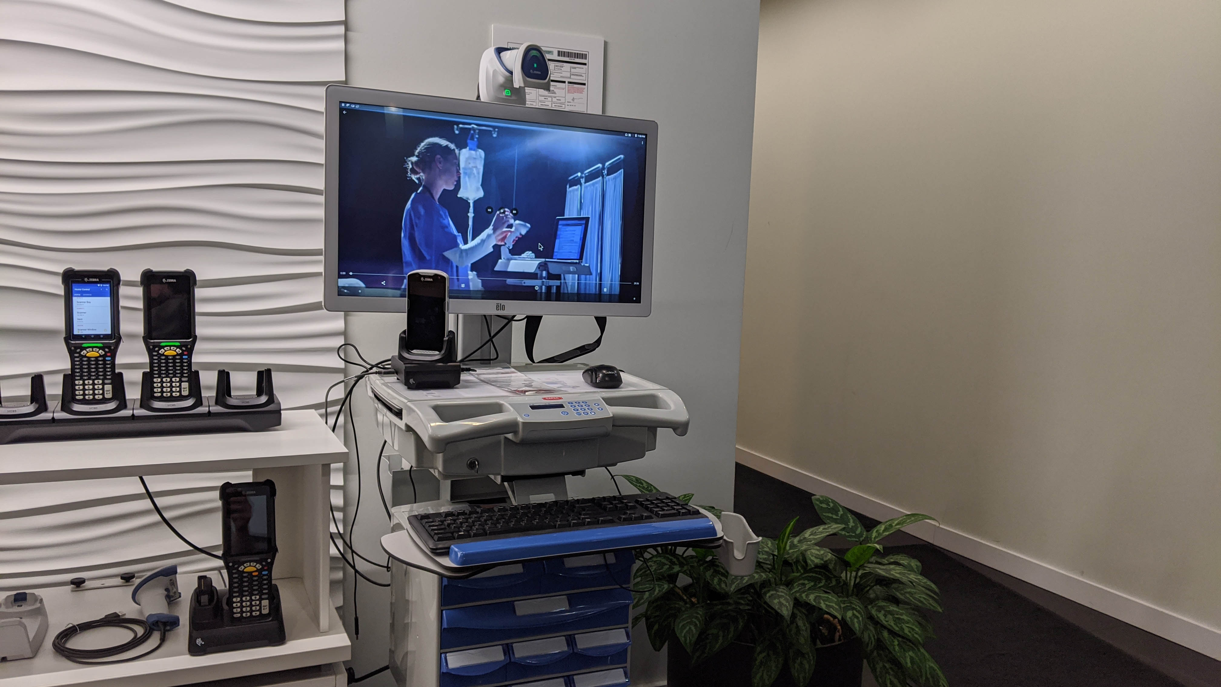 A workstation on wheels  display shows a nurse assisting a patient in another room.